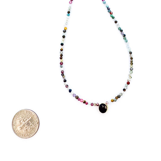 Multicolored beaded necklace with a black pendant next to a coin for size comparison on a white background