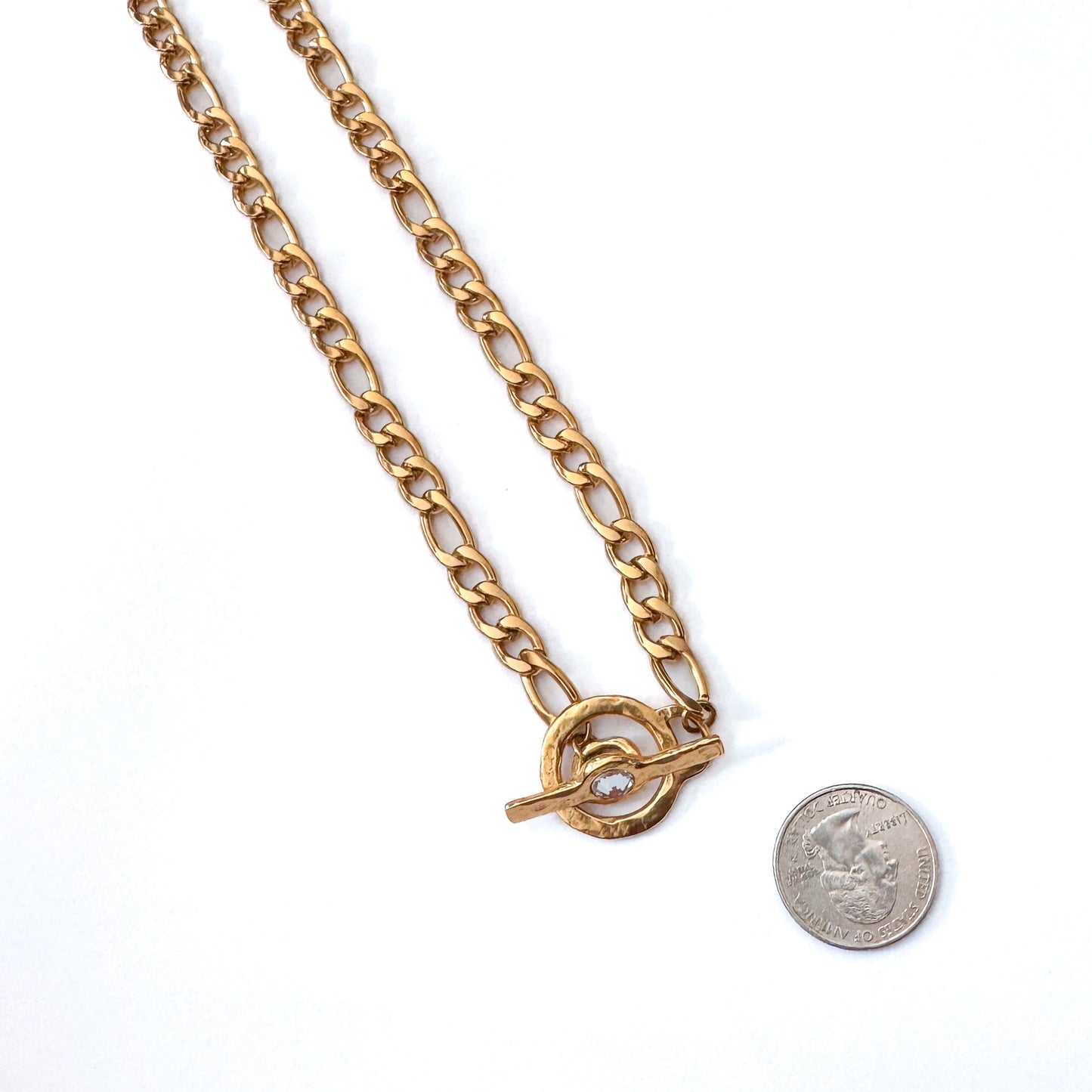 Gold chain necklace with a toggle clasp next to a dimevfor size comparison on a white background