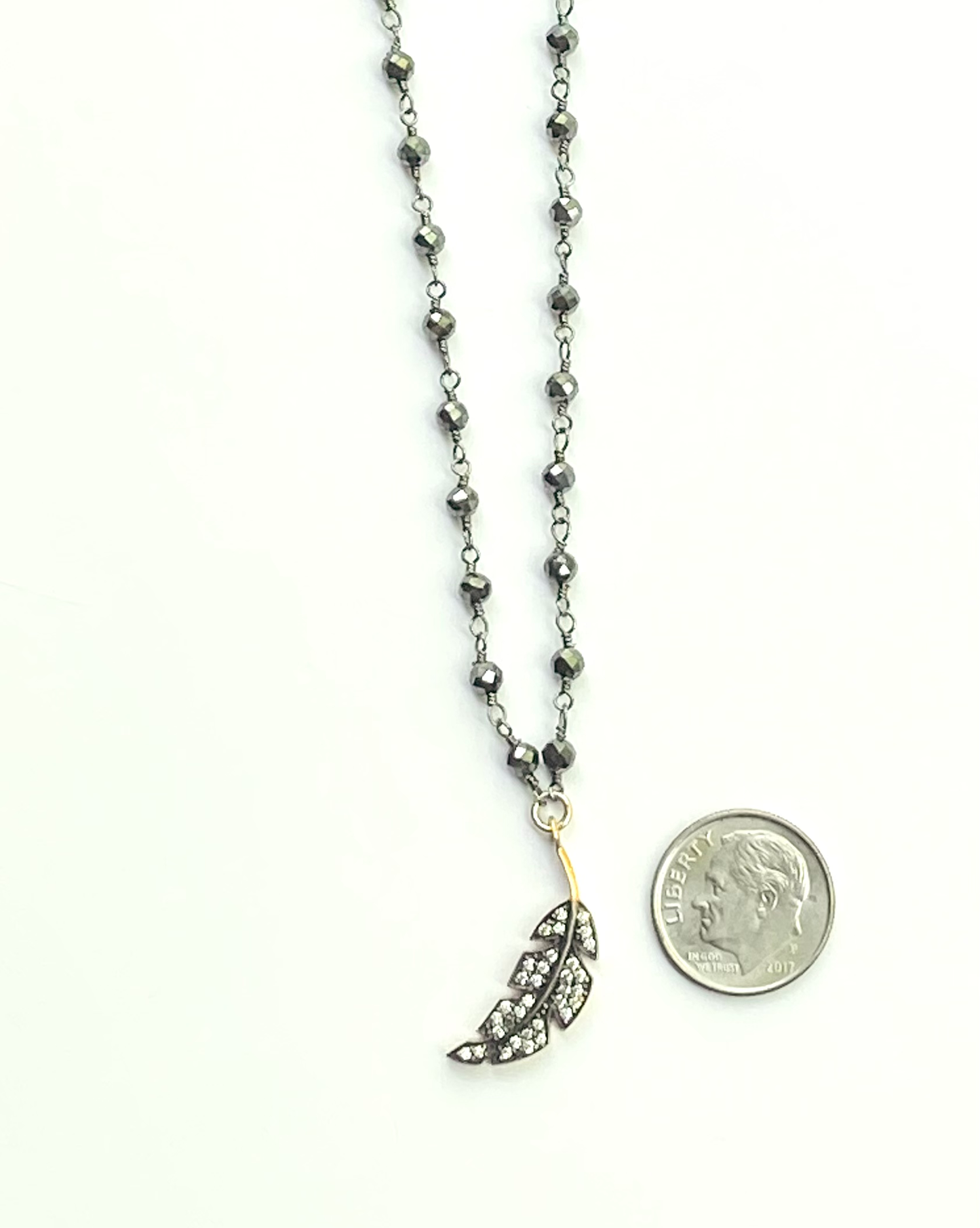 Necklace with a feather pendant next to a quarter for scale on a white background