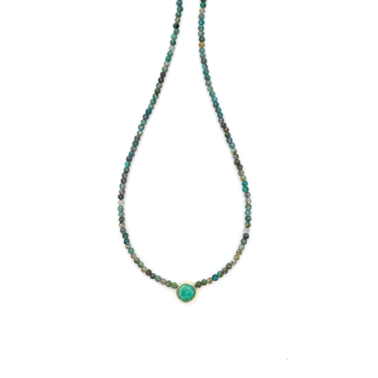 Necklace with small beads and a central green stone on a white background