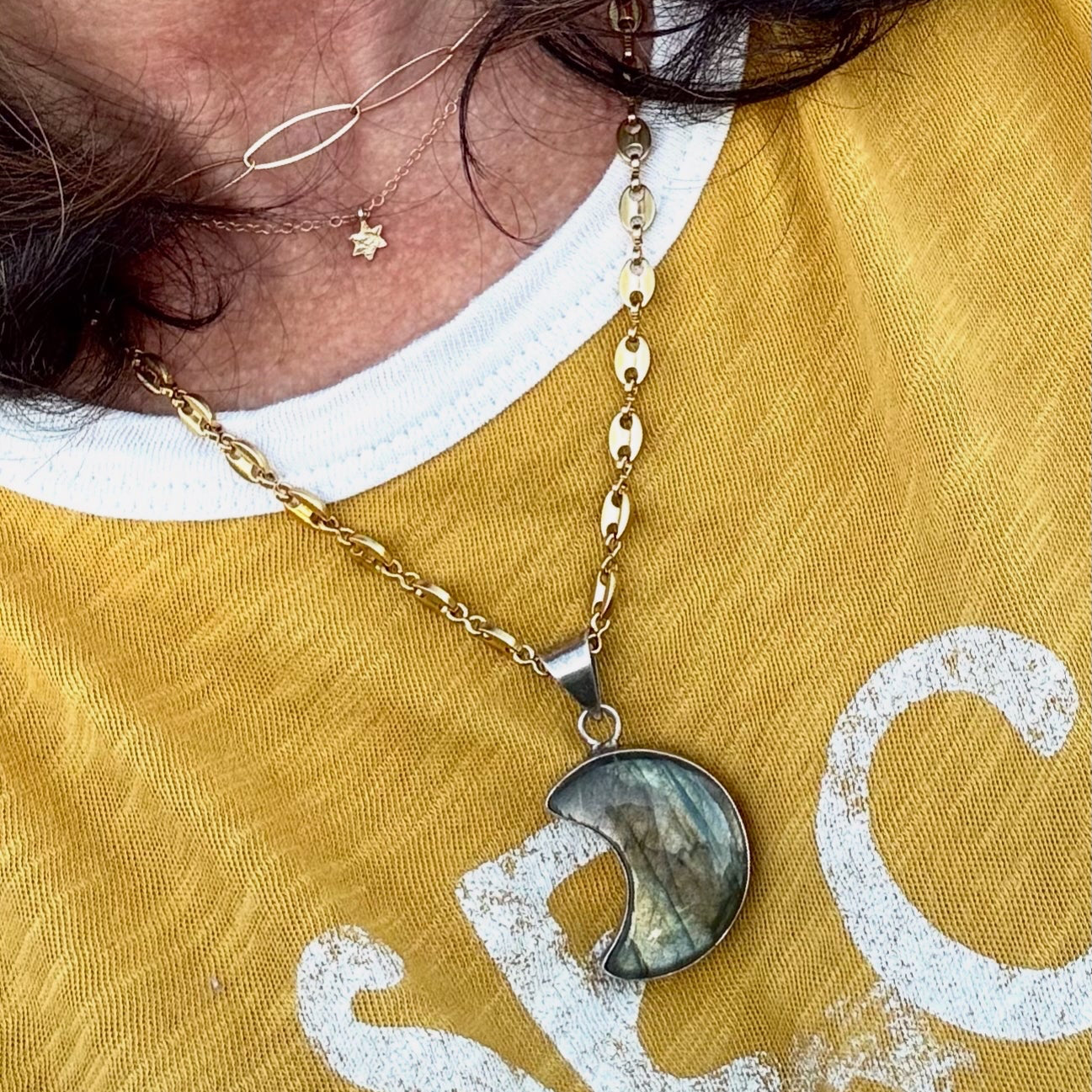 Person wearing a gold necklace with a moon pendant on a yellow shirt.