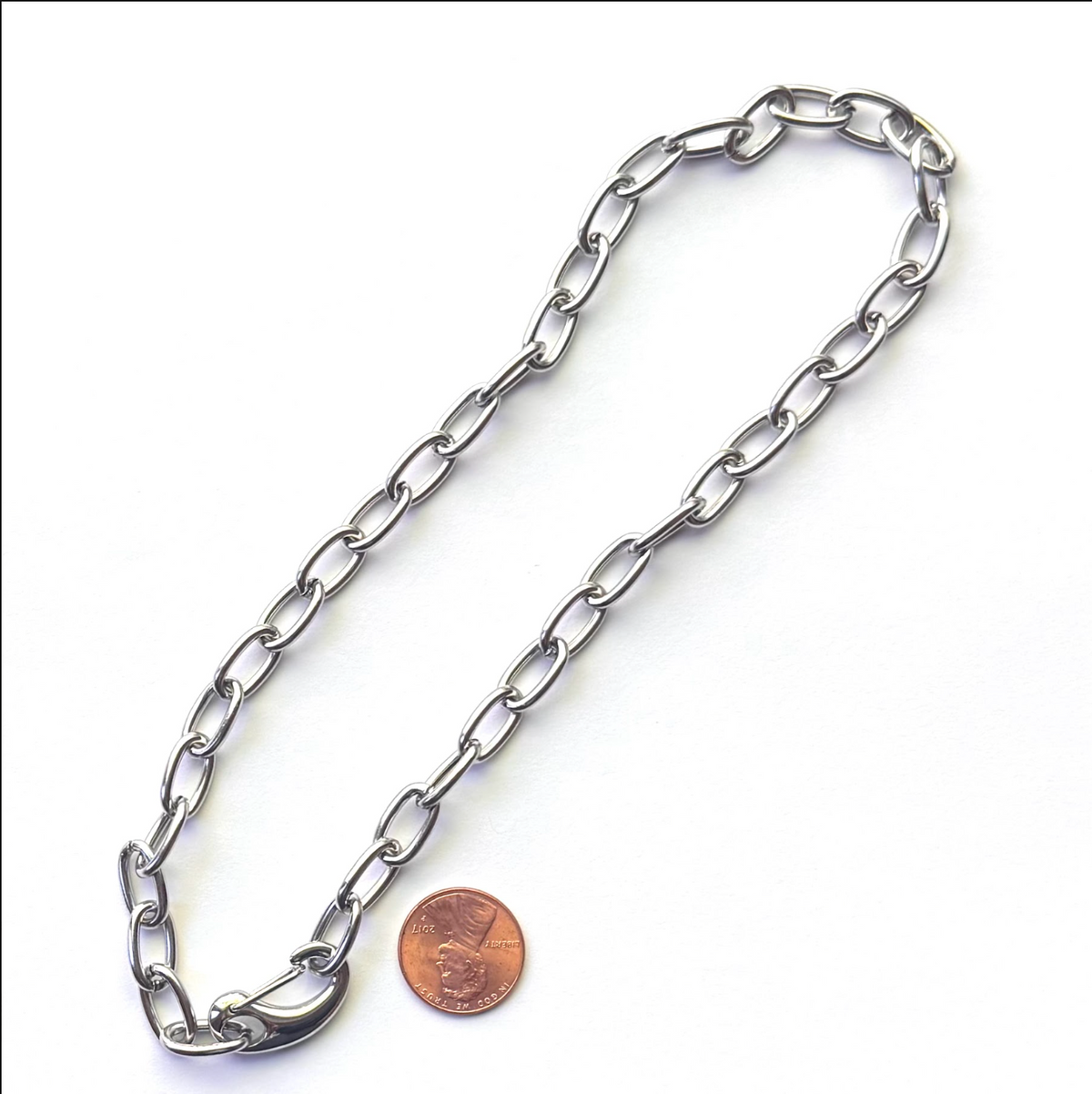 A silver metal link chain laid out on a white background, with a penny placed beside it for scale.