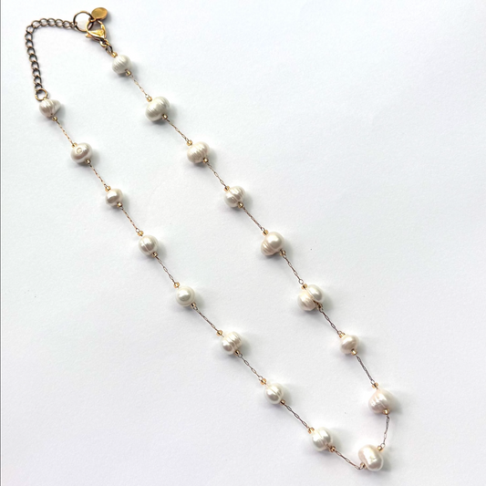 A delicate gold chain necklace featuring irregular white freshwater pearls spaced along the chain, complete with a lobster clasp and extender chain, displayed on a clean white background.