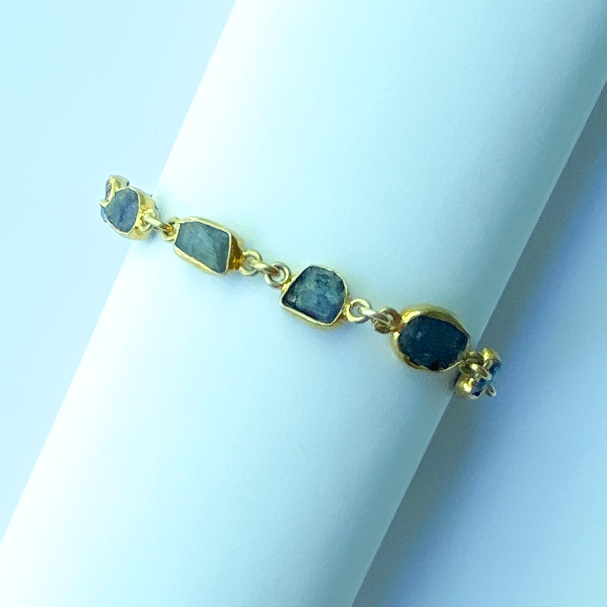 Gold bracelet with purple stones on a white stand against a light blue background