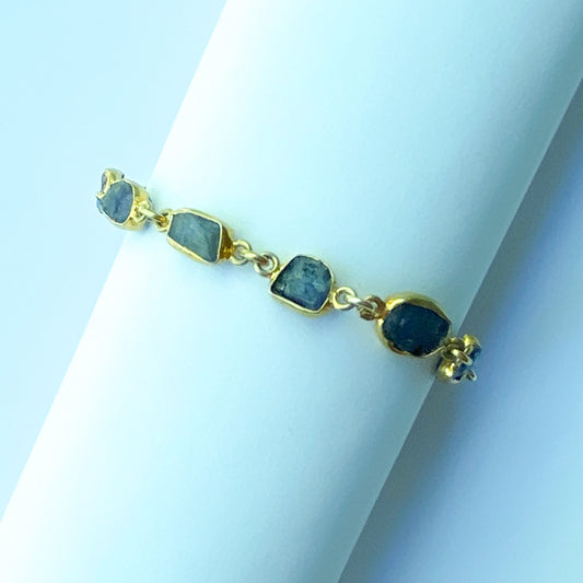 Gold bracelet with purple stones on a white stand against a light blue background