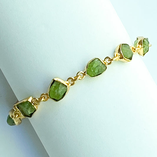 Gold bracelet with green gemstones on a light blue background