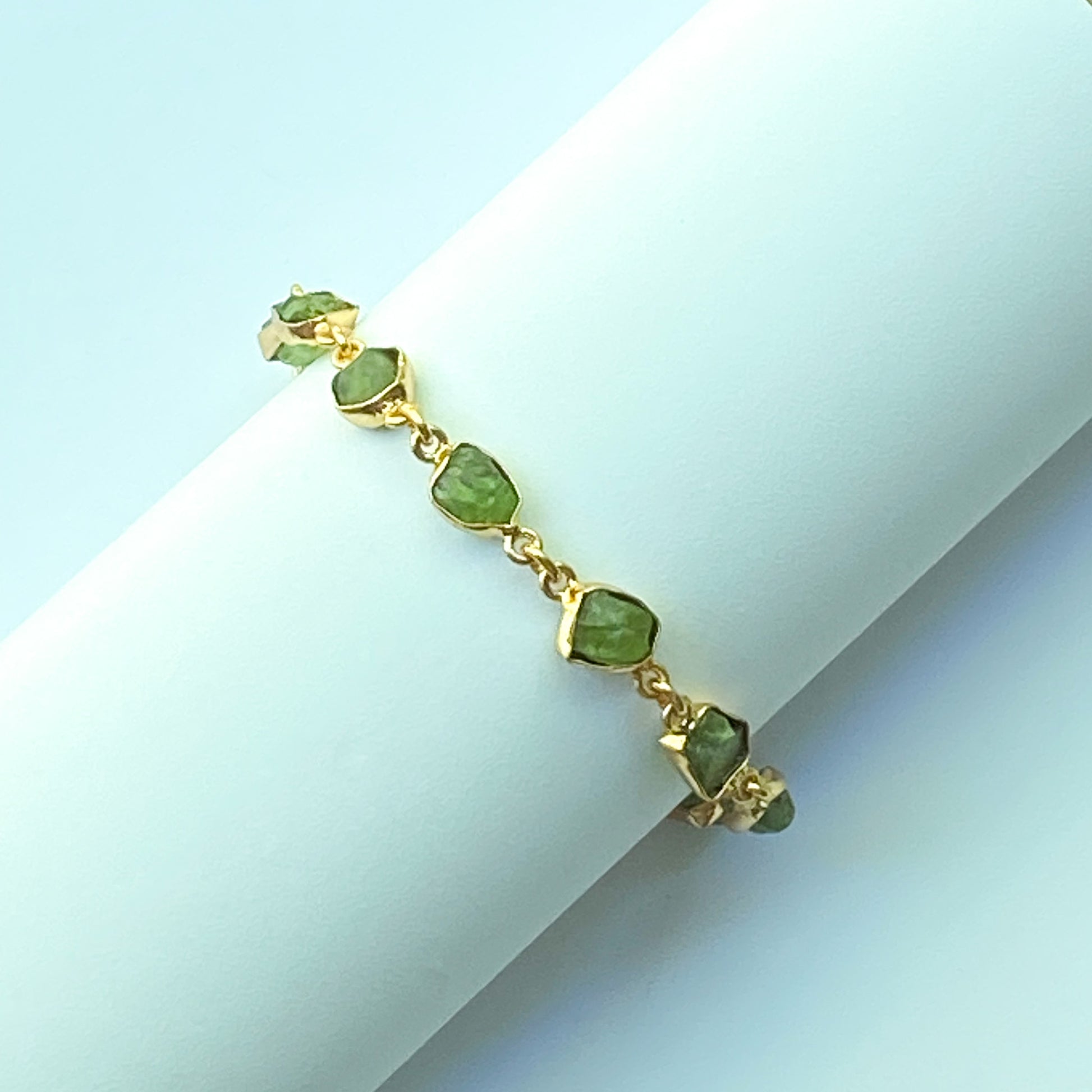 Gold bracelet with green gemstones on a light blue background
