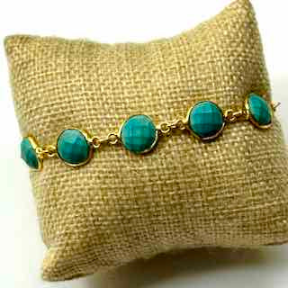 Turquoise bracelet on a gold chain displayed on a textured beige pillow