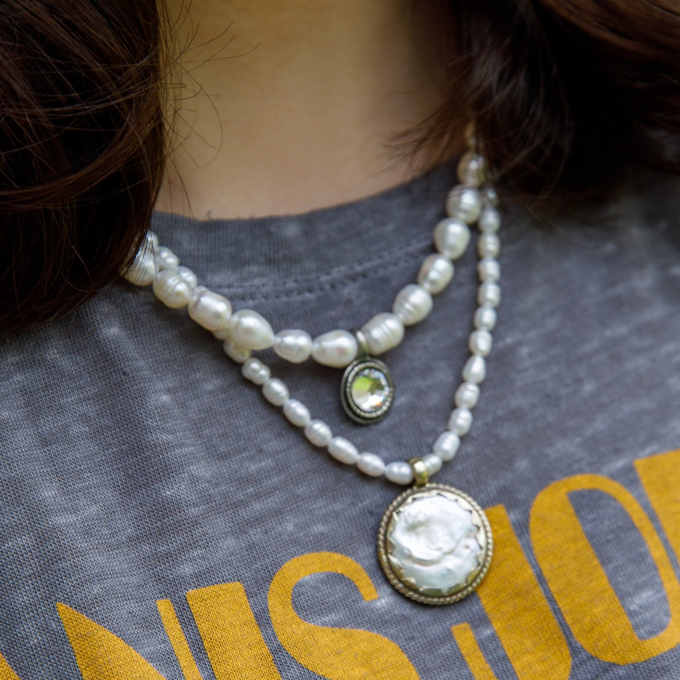 Pearl necklace with a pendant on a person wearing a gray shirt with yellow text.