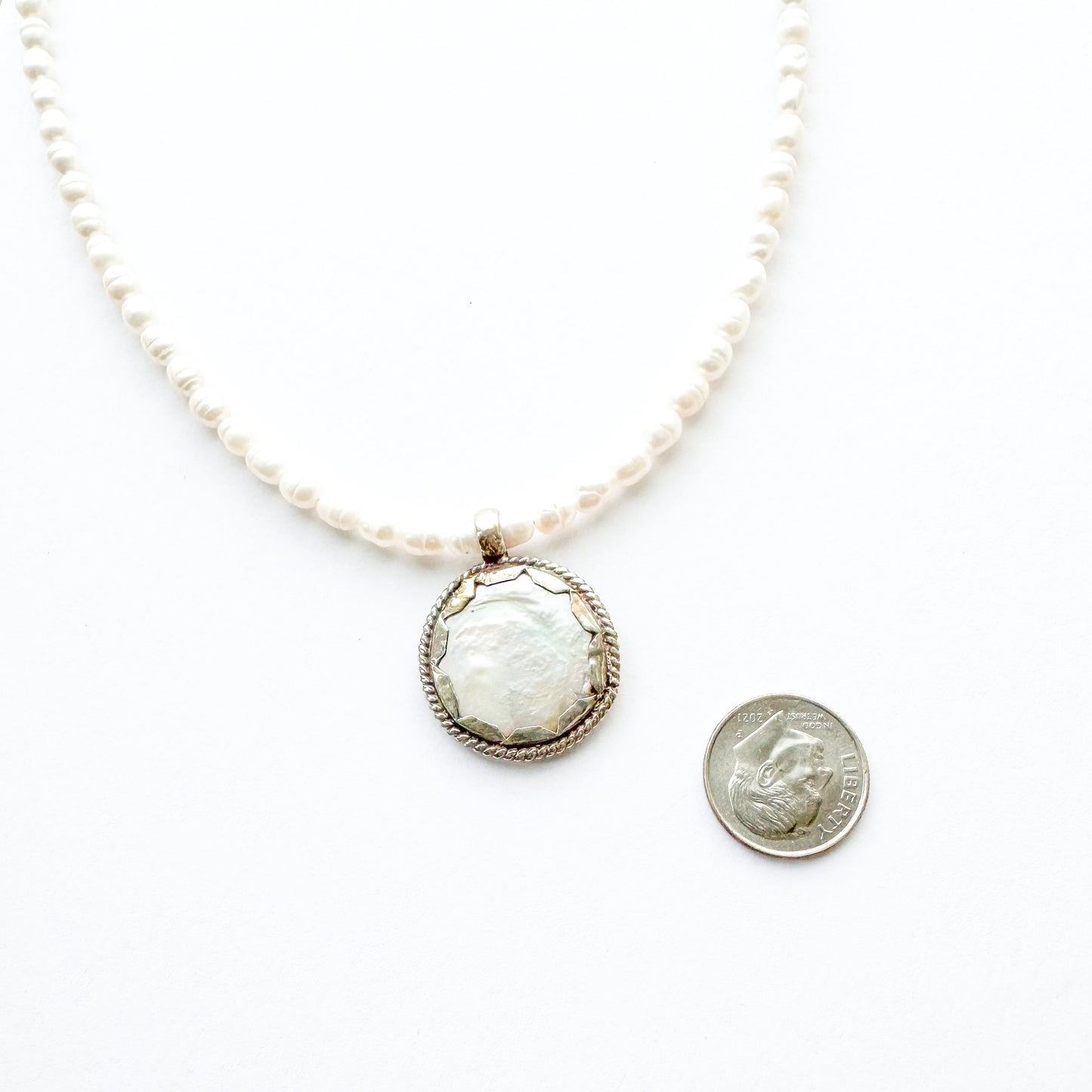 Pearl necklace with a large central pendant next to a quarter for scale on a white background