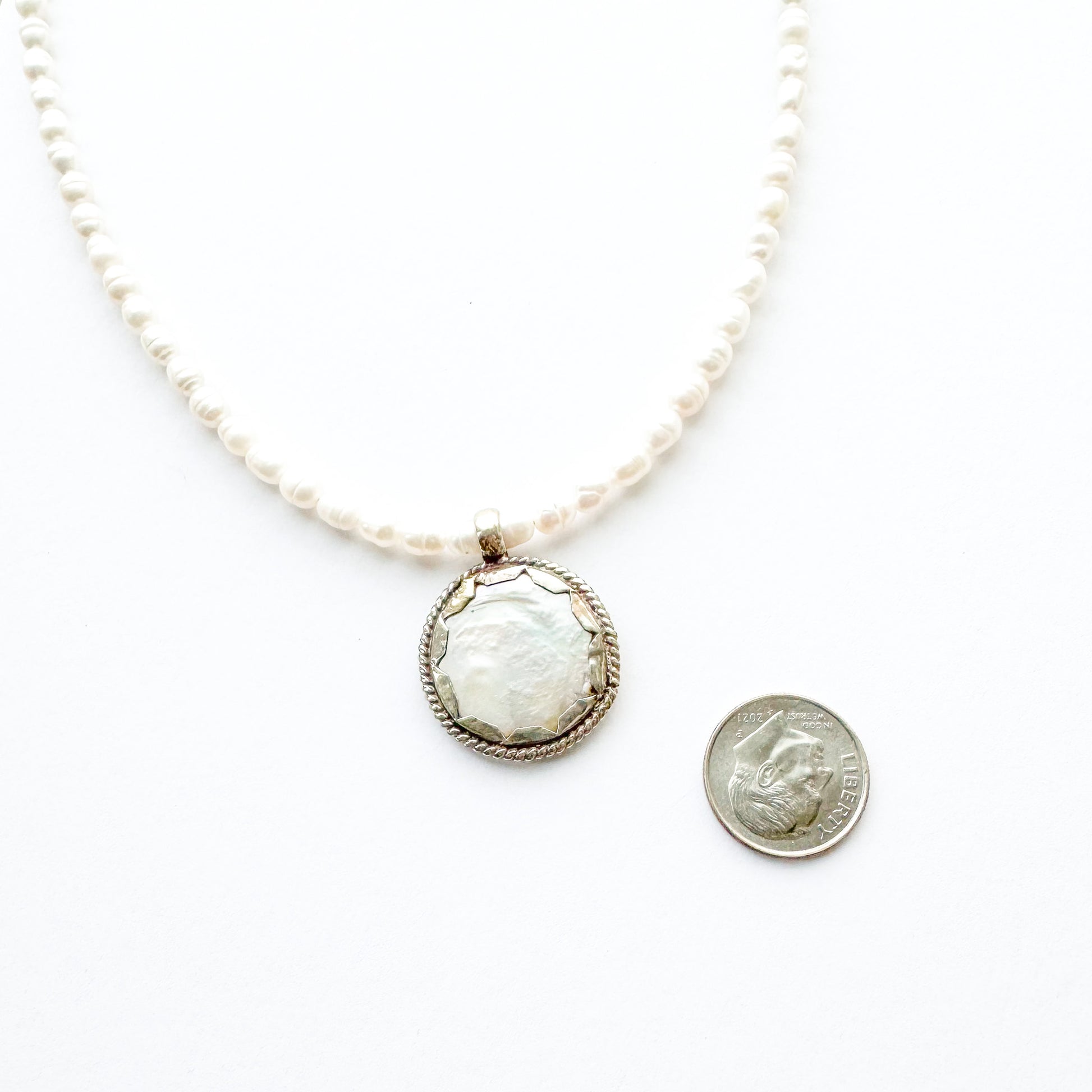 Pearl necklace with a large central pendant next to a quarter for scale on a white background