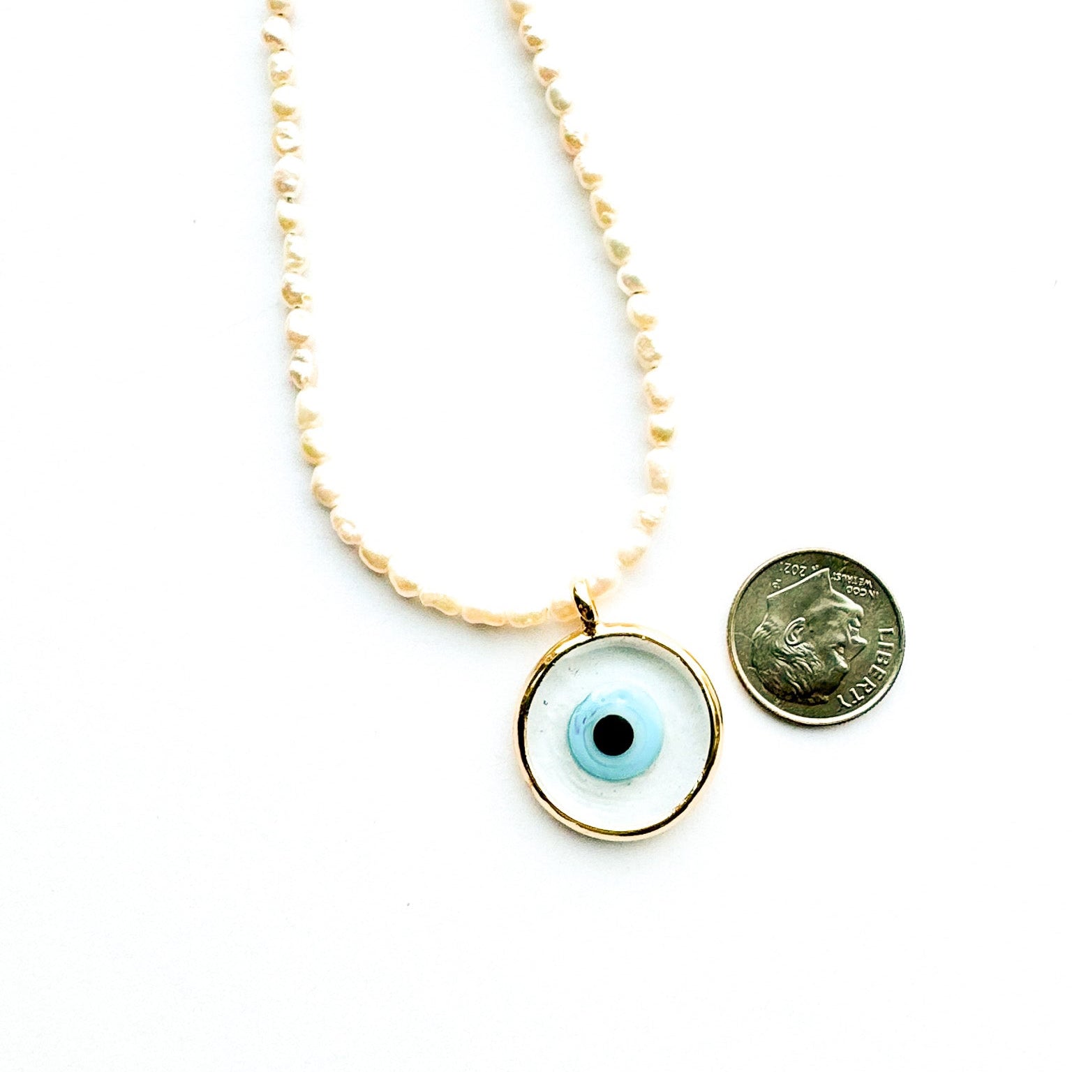 Necklace with an eye-shaped pendant next to a coin for scale on a white background