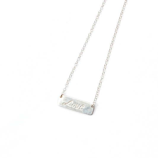 Silver necklace with a bar pendant engraved with 'LOVE' on a white background