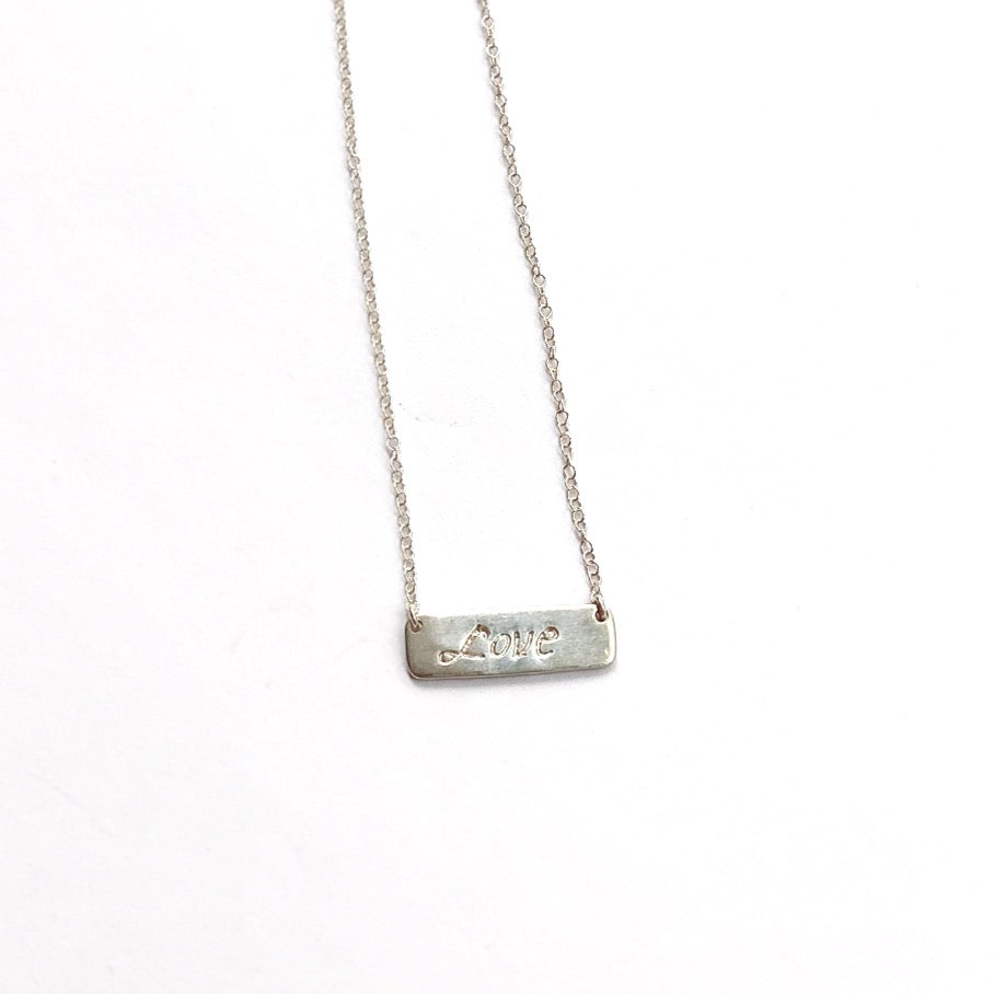 Silver necklace with 'love' pendant on a white background