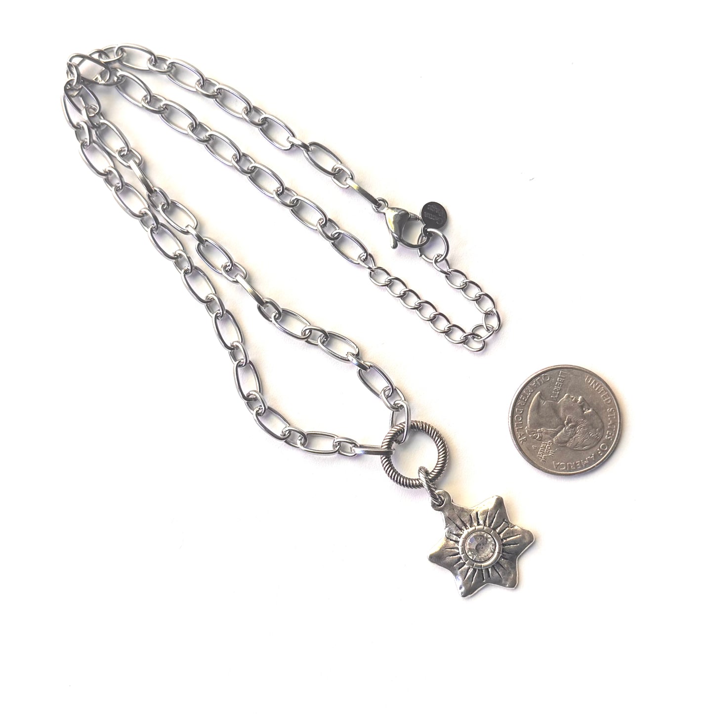 A silver-toned chain necklace with a starburst pendant, displayed on a white background next to a coin for scale.