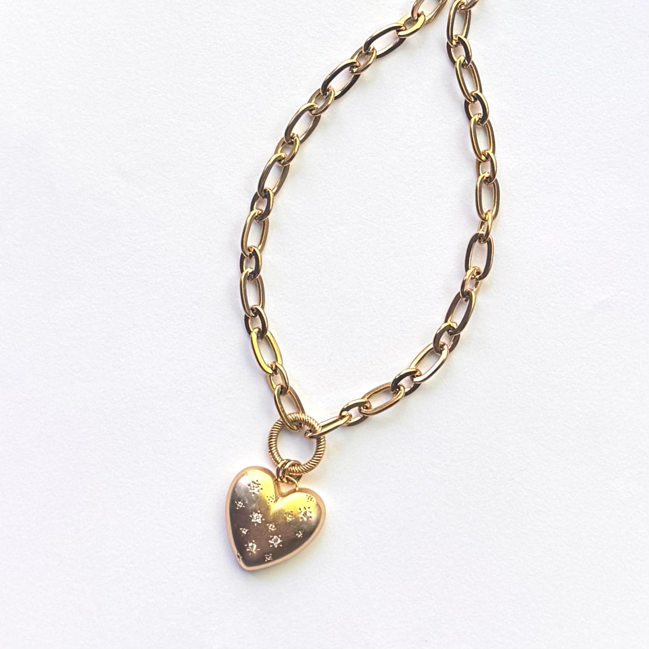 A gold-toned paperclip chain necklace with a small heart-shaped pendant featuring a starry night sky pattern, displayed on a clean white background.