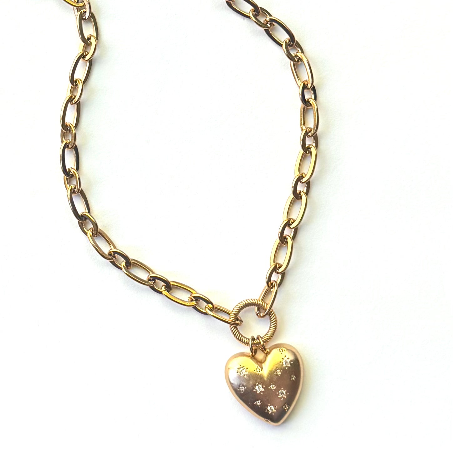 A gold chain necklace with a heart-shaped pendant featuring small star engravings, displayed on a clean white background.