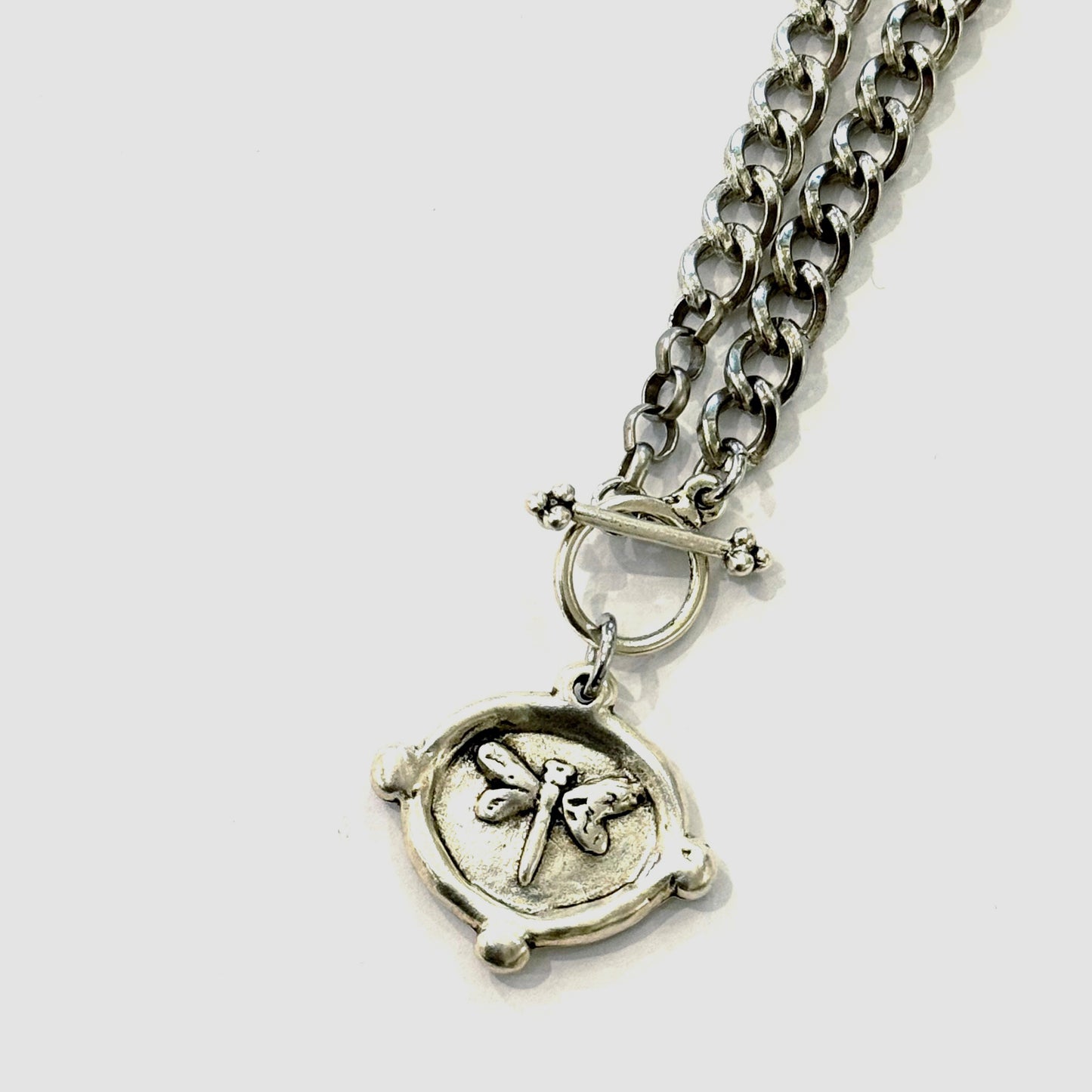 Silver chain necklace with a round pendant featuring a dragonfly design on a white background