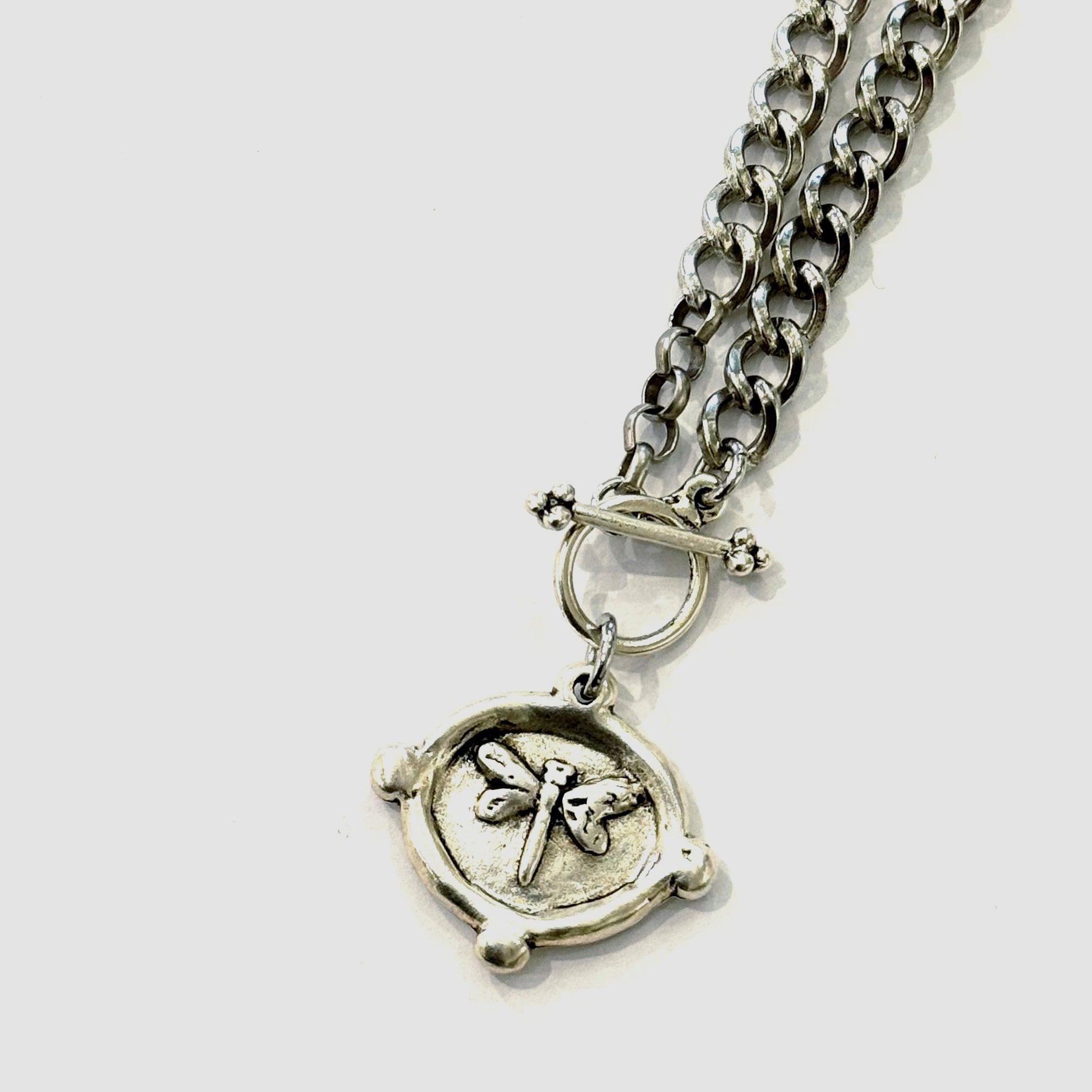 Silver chain necklace with a round pendant featuring a dragonfly design on a white background