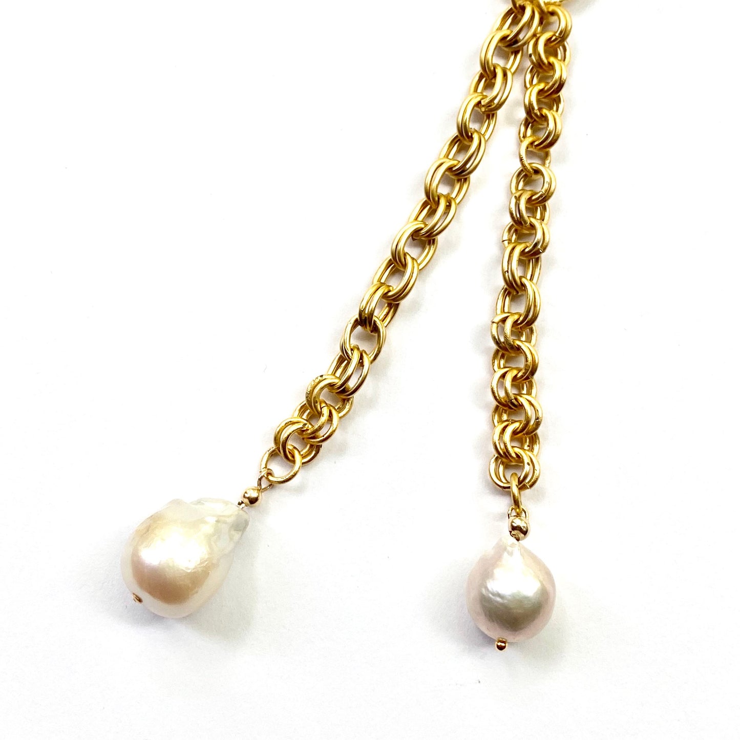Gold chain necklace with two pearl pendants on a white background