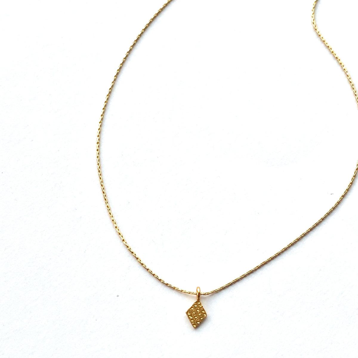 Gold necklace with a kite-shaped pendant on a white background